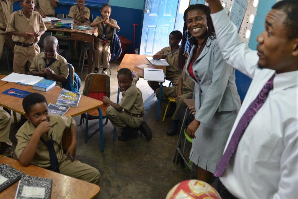 In this February 2, 2015 photo, student teacher Shane Sinclair, right, helps veteran teacher Lillia Lewin-Robinson teach third-grade boys a math lesson using a soccer ball at a co-ed primary school experimenting with single-sex classrooms in a poor c