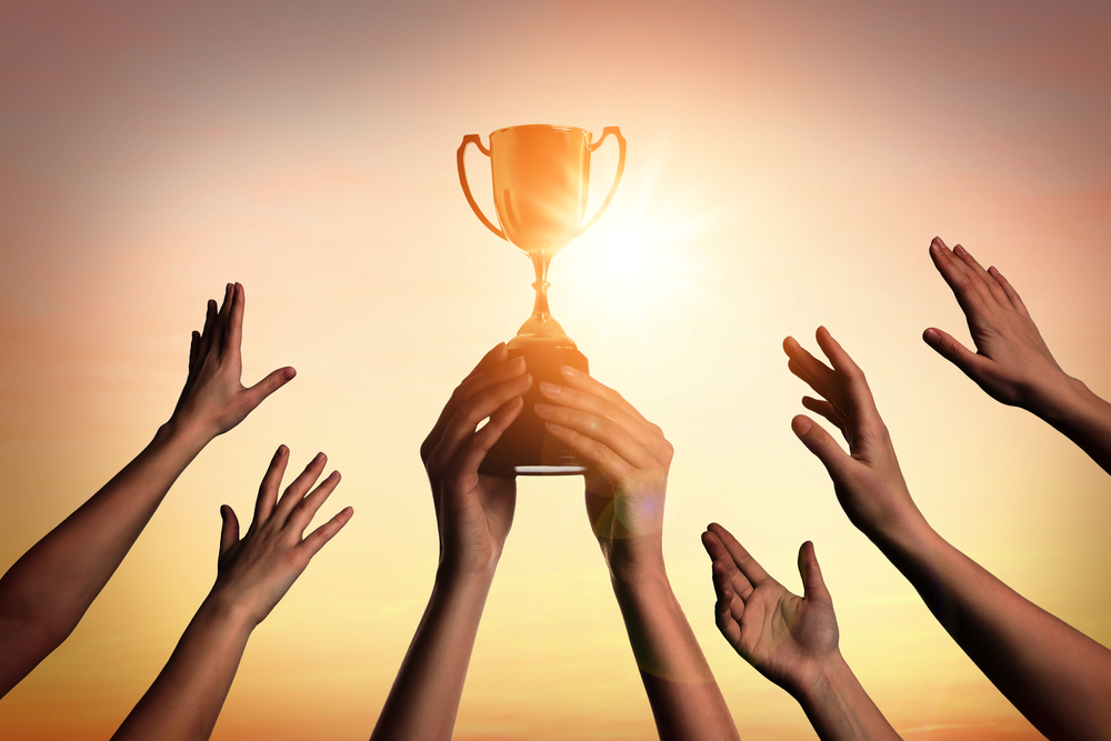 Winning,Team,With,Gold,Trophy,Cup,Against,Shining,Sun,In